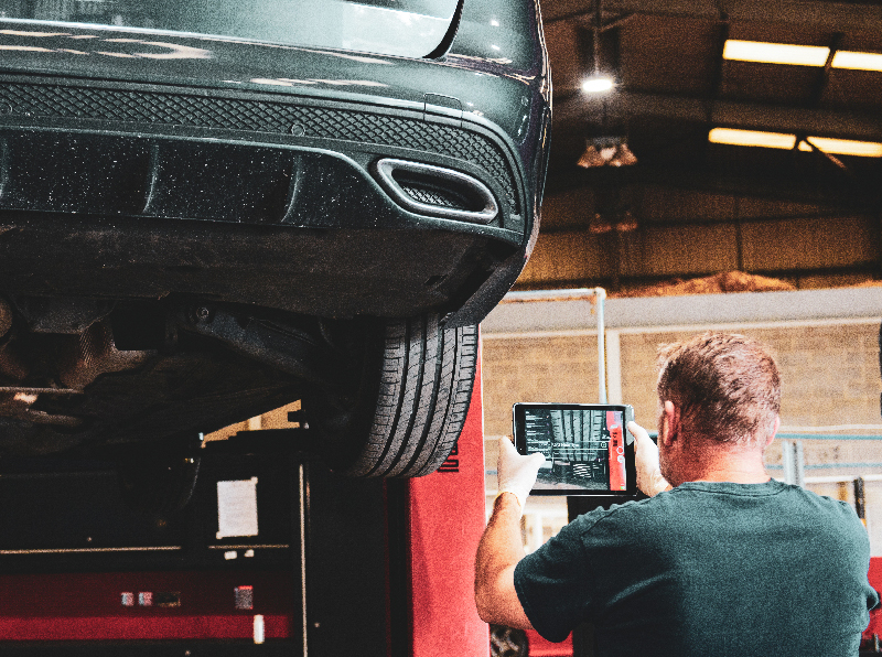 Vehicle technician using ipad to check tyre tread as part of a vehicle health check.