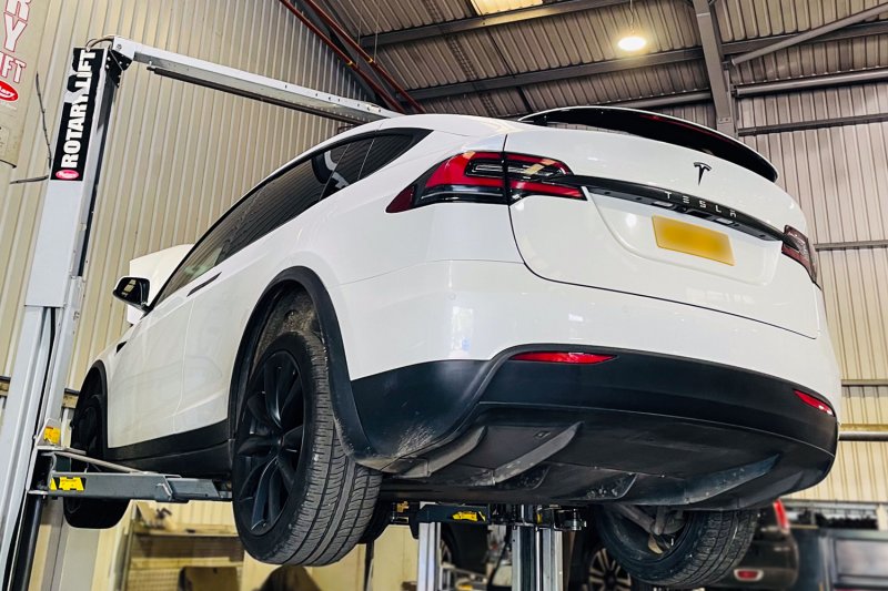 White tesla on a ramp, back view with the bonnet open at the front