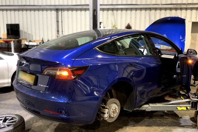 Blue Tesla on a ramp with wheels off and bonnet open ready for repairs