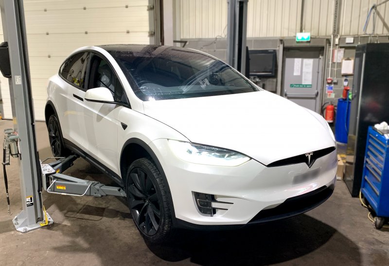 White Tesla lifted on a ramp from a front view.